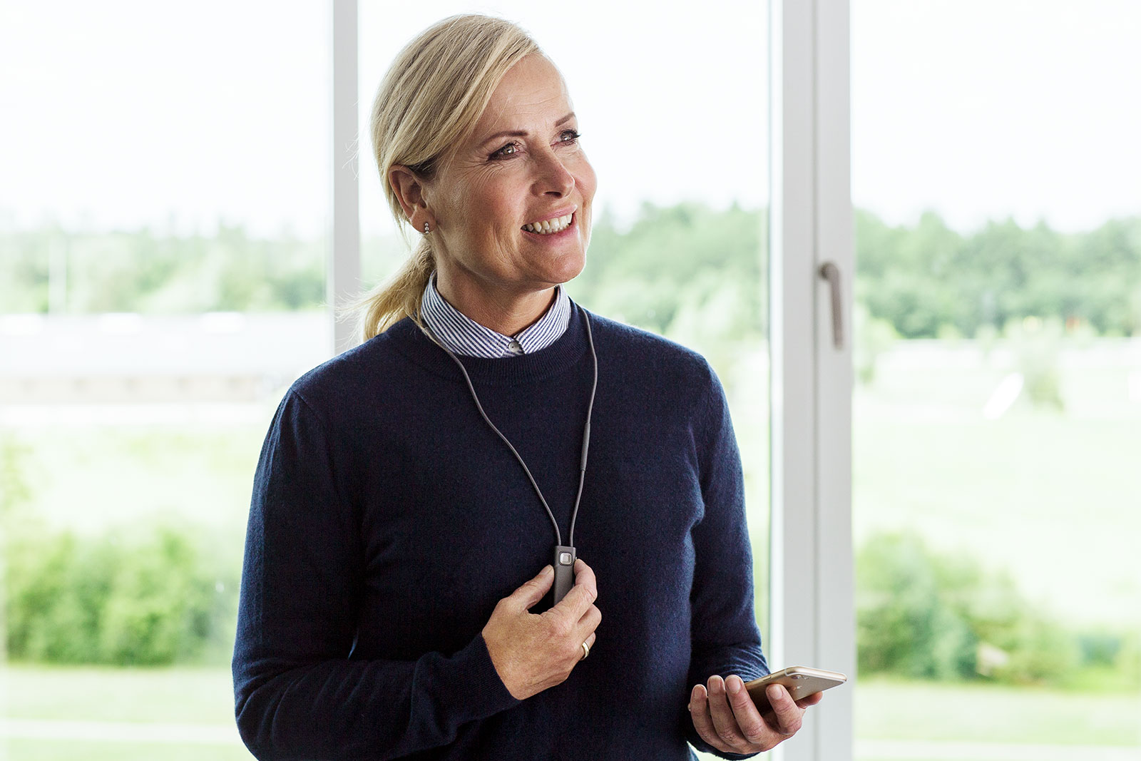 Woman holding COM-DEX hearing aid accessory and phone